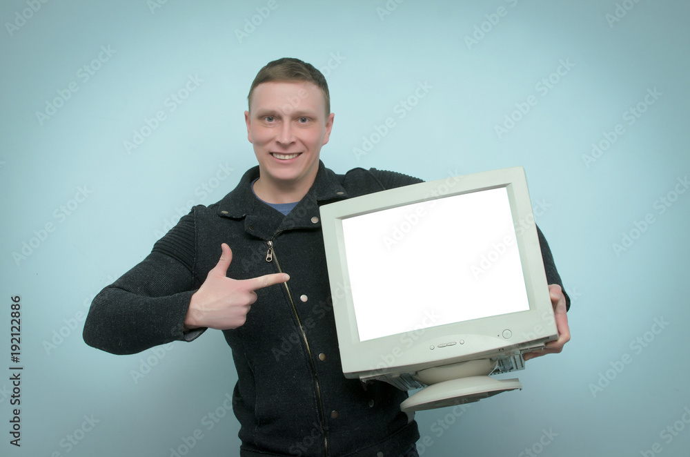 Happy cheerful man is holding in hands a old computer monitor with blank screen and is showing on it by his index finger isolated on blue background. Happy cheerful man is holding in hands a old computer monitor with blank screen and is showing on it by his index finger isolated on blue background.