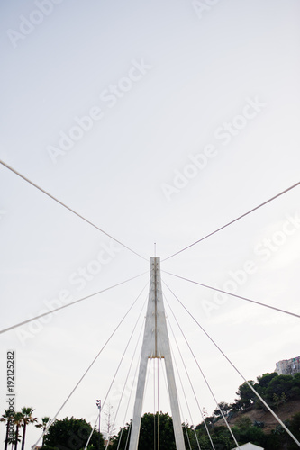 Tall white bridge in a city. Close-up photo of its ropes.