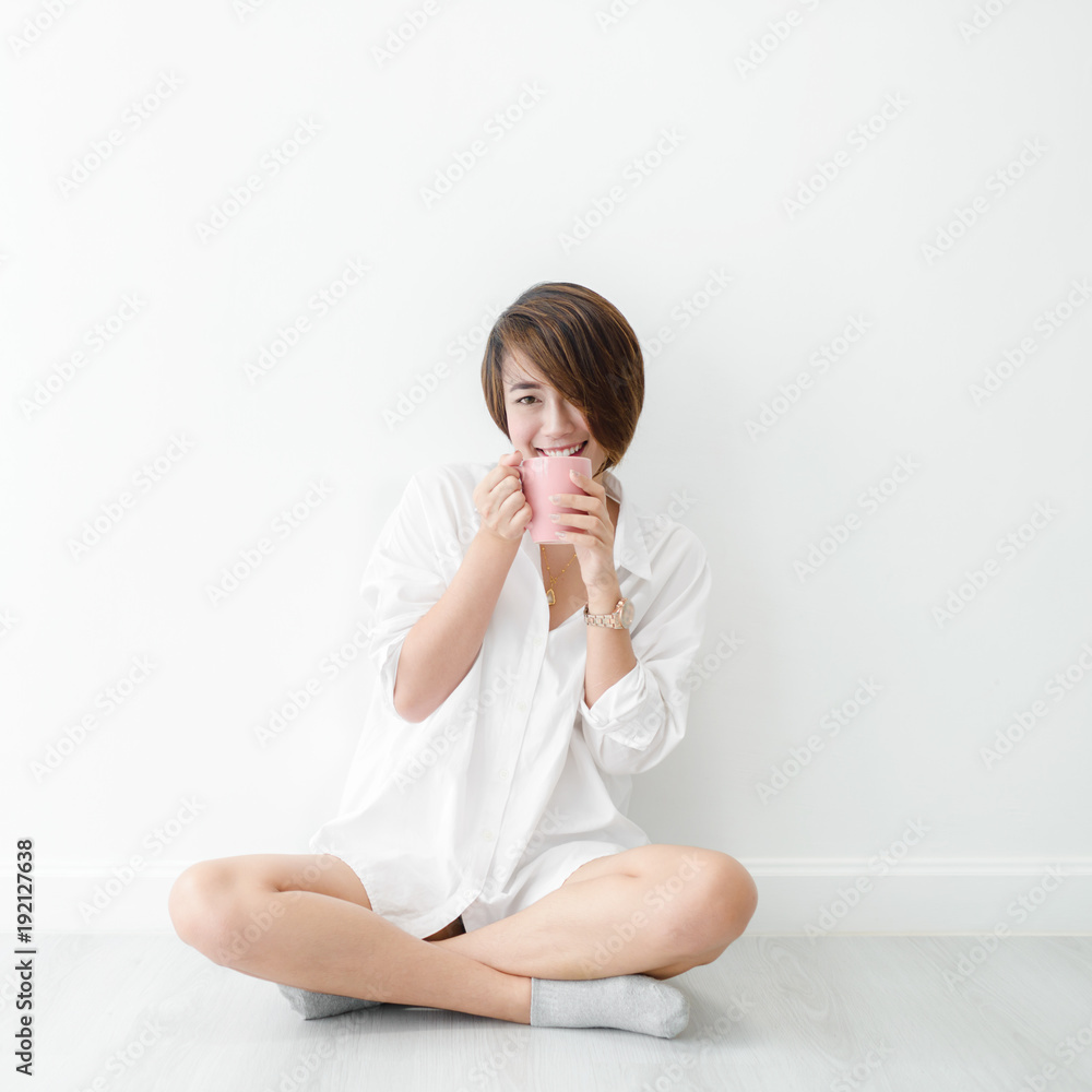 Happy Asian woman wearing white shirt holding pink mug in white room. Happy Asian woman wearing white shirt holding pink mug in white room.