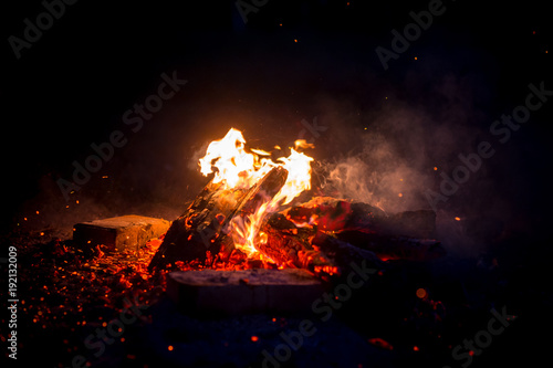 Burning wood at night. Campfire at touristic camp at nature in mountains. Flame amd fire sparks on dark abstract background. Cooking barbecue outdoor. Hellish fire element. Fuel  power and energy.