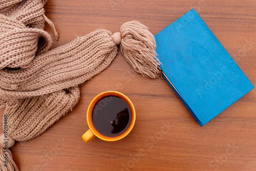 Cup of coffee, knitted scarf and book on wooden background