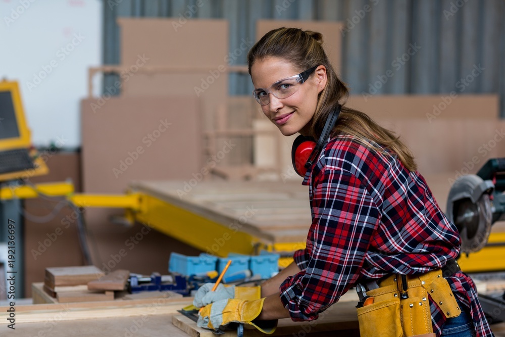 Female carpenter marking on wooden plank with pencil Female carpenter marking on wooden plank with pencil