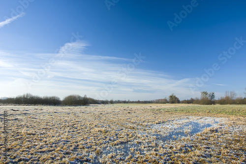 Frost on a wet meadow and white clouds