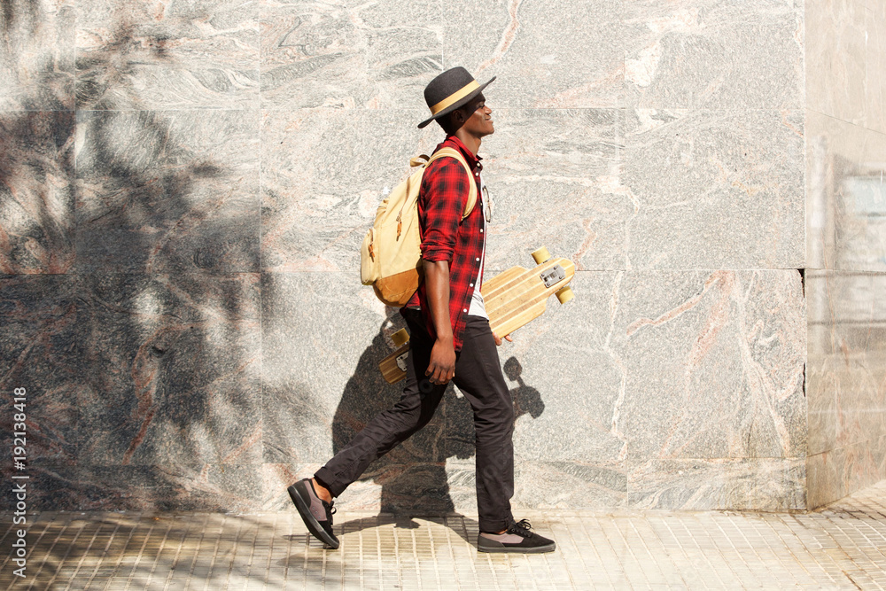 Obraz premium side portrait of young african american man walking outside with skateboard