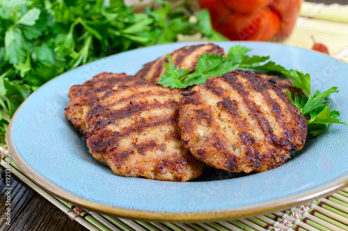 Juicy cutlets, fried on a grill in a ceramic plate and canned tomatoes on a wooden background.