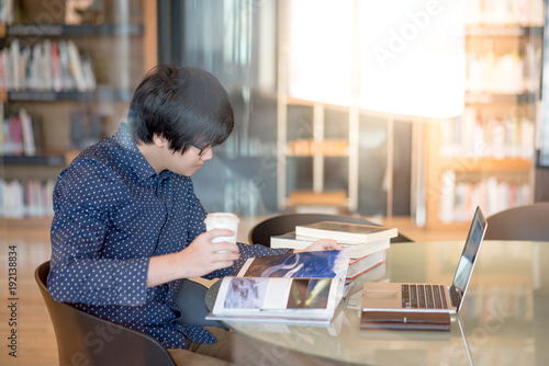 Young Asian man student reading book and magazine in public library, education research and self learning in university life concepts