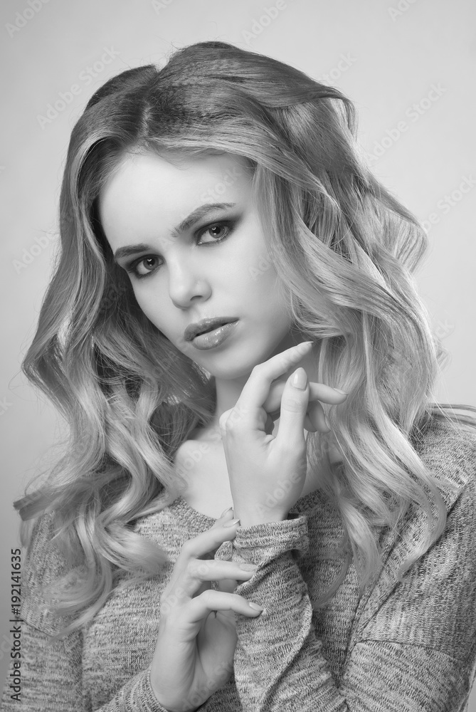 Portrait of blonde girl with makeup and long curls in gray sweater on gray background black and white image. Portrait of blonde girl with makeup and long curls in gray sweater on gray background black and white image.
