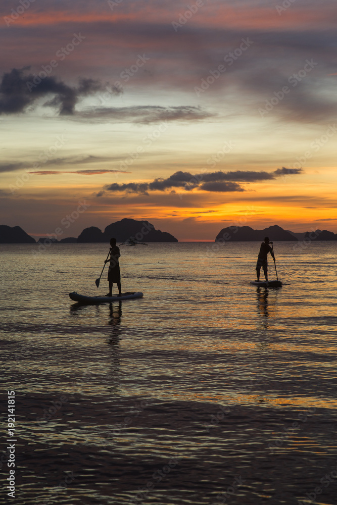 Fototapeta premium two man silhouette standing on sup boards on sunset time in El Nido, Palawan, Philippines, Corong Corong beach