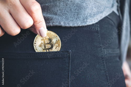 Closeup image of a woman picking up and dropping bitcoin into a black jean pocket