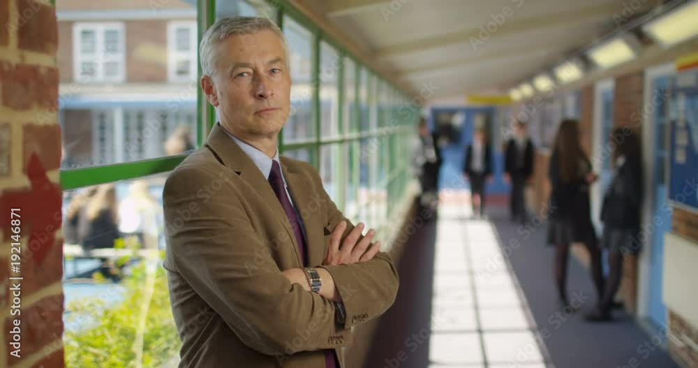 4K Portrait serious school headmaster with arms crossed & students chatting in background. Slow motion 4K Portrait serious school headmaster with arms crossed & students chatting in background. Slow motion