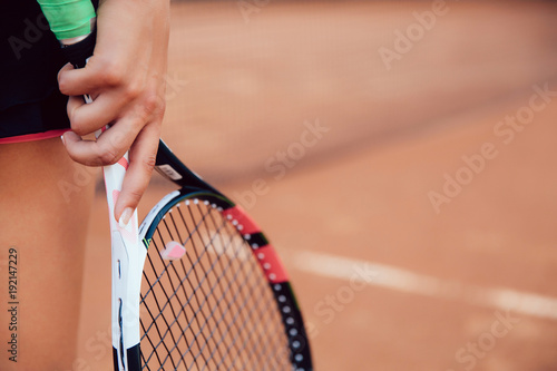 Woman holding tennis racket on clay court. Close-up view of female hand and racquet.