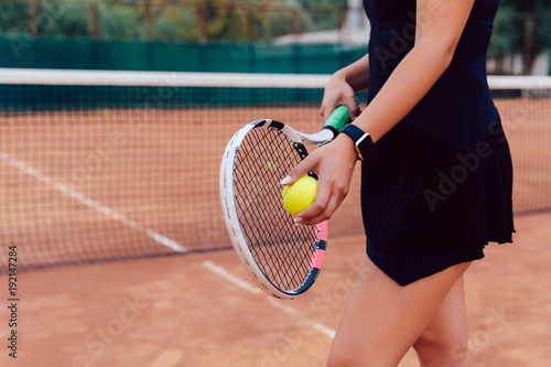 Tennis player. Close-up photo of athlete woman in sportswear holding racket and ball, playing tennis on the court.