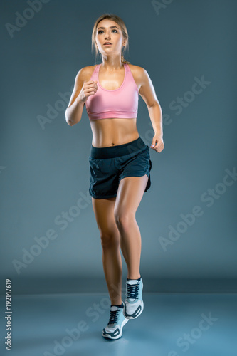 Young beautiful woman in fitness wear runs over blue grey background. The athlete runs to the camera and looks up. An inspired girl runs to meet her dream © Volodymyr Shcerbak