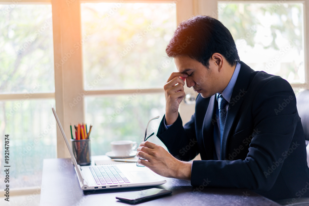 Exhausted tired young asian businessman working on laptop at office, massaging nose bridge and holding glasses. Exhausted tired young asian businessman working on laptop at office, massaging nose bridge and holding glasses.