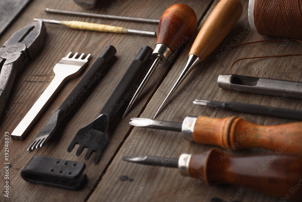 Set of leather craft tools on wooden background. Workplace for shoemaker. Piece of hide and working handmade tools on a work table. Set of leather craft tools on wooden background. Workplace for shoemaker. Piece of hide and working handmade tools on a work table.