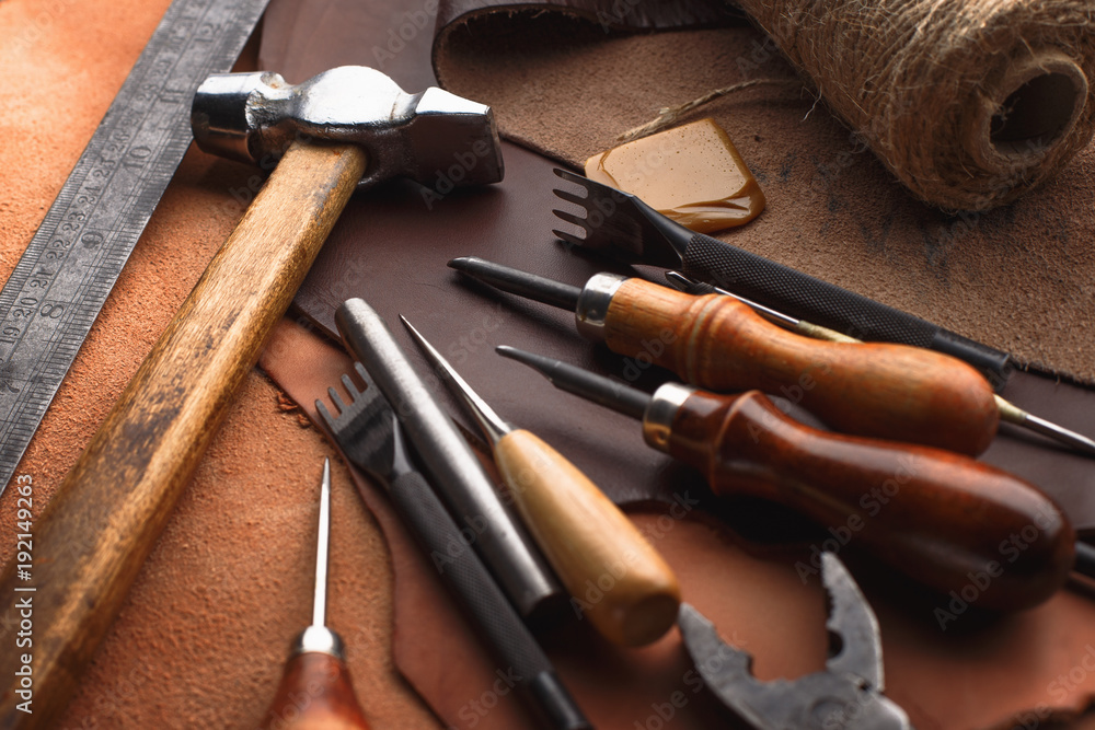 Set of leather craft tools on wooden background. Workplace for shoemaker. Piece of hide and working handmade tools on a work table. Set of leather craft tools on wooden background. Workplace for shoemaker. Piece of hide and working handmade tools on a work table.