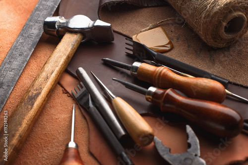 Set of leather craft tools on wooden background. Workplace for shoemaker. Piece of hide and working handmade tools on a work table.