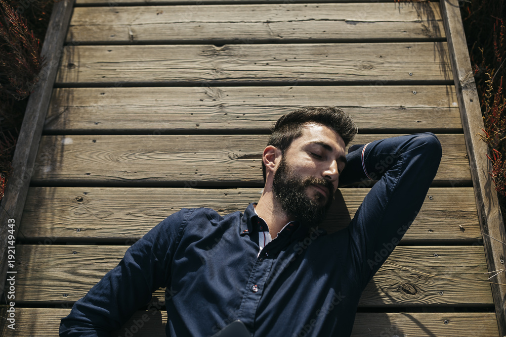 Man enjoying peace on rural pierMan with eyes closed lying on wooden pier in sunlight dreaming and lounging alone after work. Man enjoying peace on rural pierMan with eyes closed lying on wooden pier in sunlight dreaming and lounging alone after work.