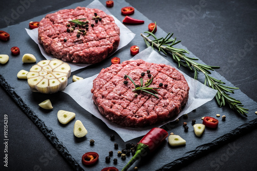 Raw cutlet of minced meat with ingredients on a dark cooking background