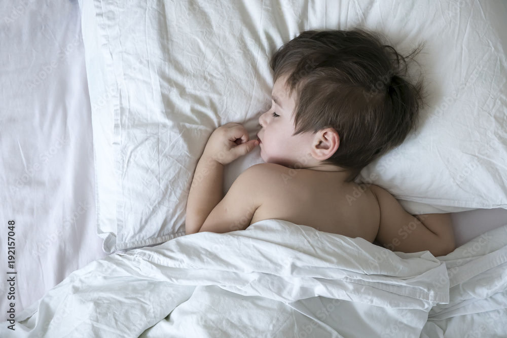 Peaceful baby lying on a bed while sleeping in a bright room. cute two year old Asian boy on white the pillow Peaceful baby lying on a bed while sleeping in a bright room. cute two year old Asian boy on white the pillow