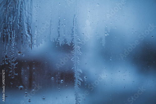 Moody picture of water drops freezing on a dirty window glass in winter in blueish evening light.