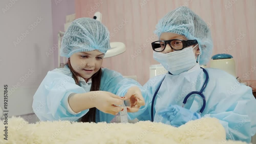a funny girl makes an injection for a teddy bear, a child represents her future profession, next to the boy who controls the treatment process at the patient a funny girl makes an injection for a teddy bear, a child represents her future profession, next to the boy who controls the treatment process at the patient