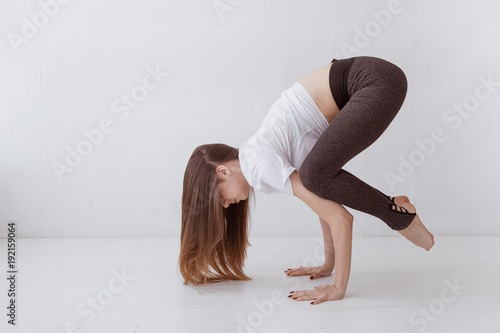 Beautiful young woman at home on a white background engaged in yoga, standing in a pose Crane (Crow) Pose, Bakasana (Kakasana), full length. Lifestyle.