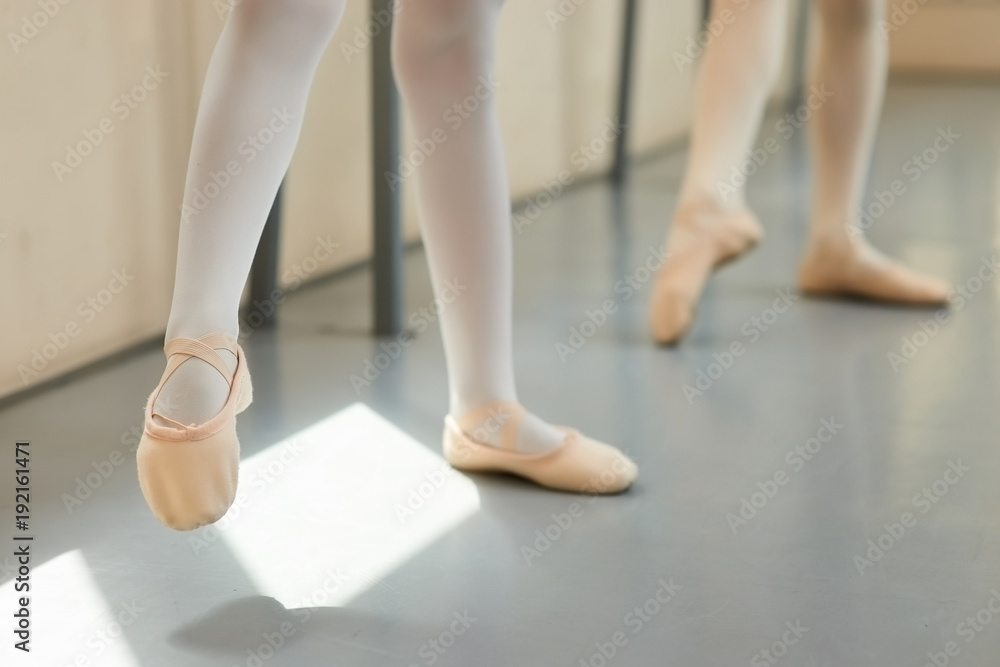 Naklejka premium Legs a little ballerina in a pink ballet shoes. Young girl in ballet pose at classical ballet school, cropped image.
