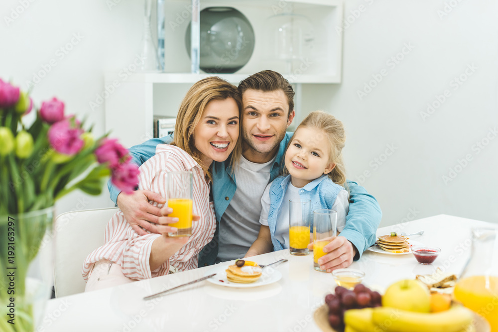 portrait of smiling parents and daughter looking at camera during breakfast at home