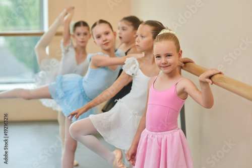 Cute ballerina in pink dress at studio. Young ballerinas in beautiful dresses standing at ballet barre in studio.