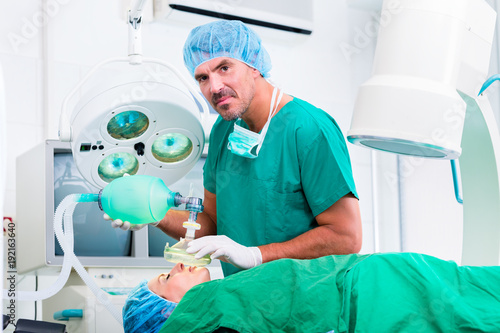 Doctor surgeon with patient in operating room applying anesthetic with mask