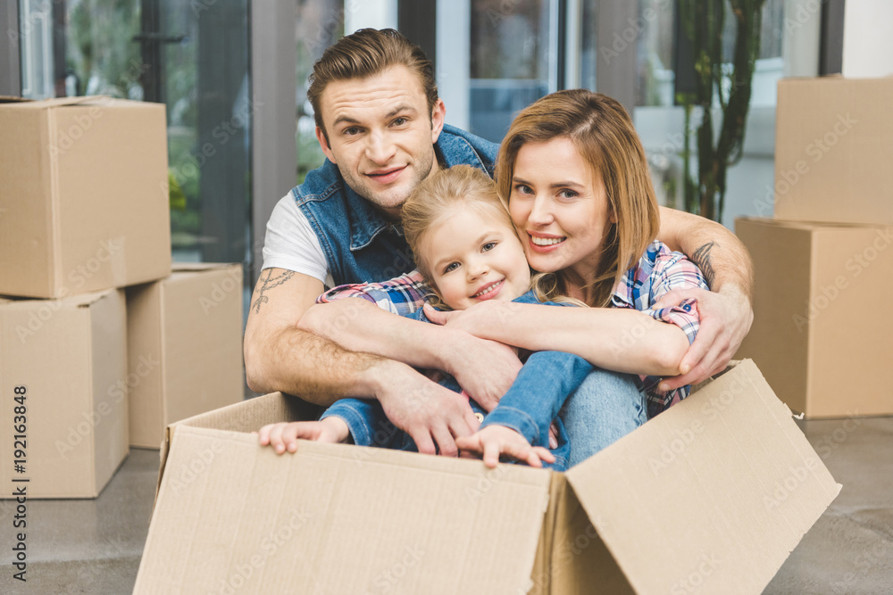 portrait of smiling parents and little daughter in cardboard box at new home, moving home concept portrait of smiling parents and little daughter in cardboard box at new home, moving home concept
