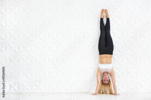 Fotografia, Obraz Young blonde woman doing a handstand over a white wall