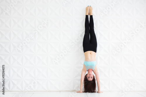 Foto Young brunette woman doing a handstand over a white wall