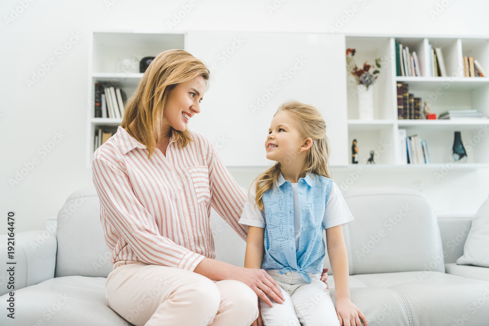 smiling daughter and mother looking at each other while sitting on sofa at home smiling daughter and mother looking at each other while sitting on sofa at home