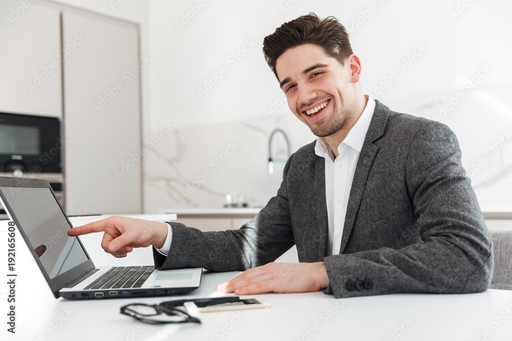 Photo of happy businesslike man pointing finger on screen of laptop, while doing telework from home