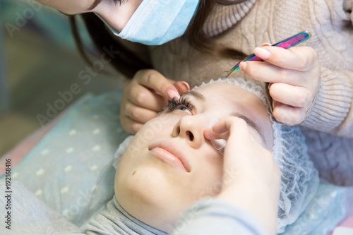 A young girl increases eyelashes in a beauty salon. The process of increasing and volumetric eyelash extensions to a blonde girl.