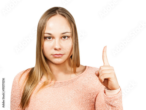 Close up portrait of beautiful smiling young woman in a beige shirt looking forward and showing pointing finger up, isolated on a white background photo