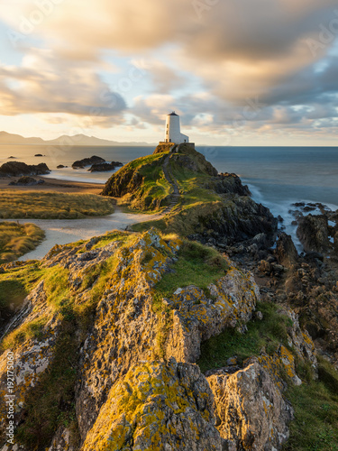 Golden morning light on rocks at Llanddwyn Lighthouse on the Anglesey Coast, Wales, UK. photo