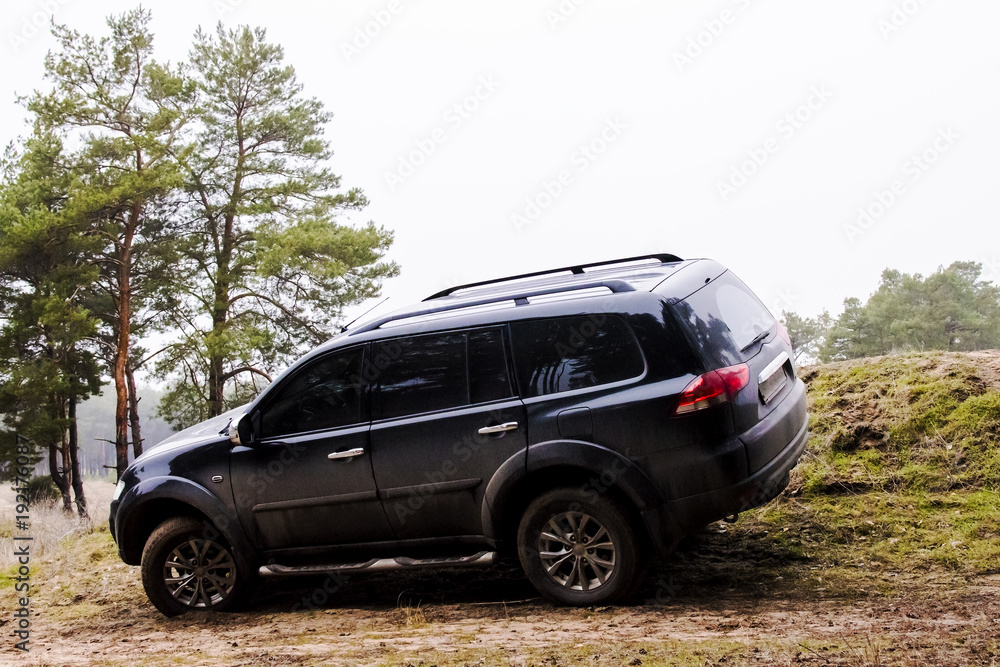 large black SUV stands inclined on a sandy hill in the forest