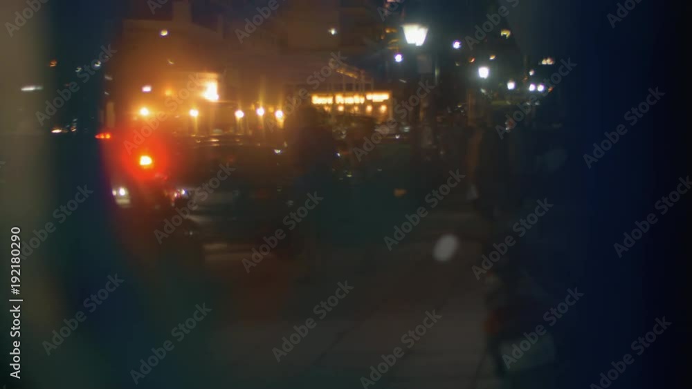 View through the glass to the evening city street with people on sidewalk and car traffic on the road View through the glass to the evening city street with people on sidewalk and car traffic on the road