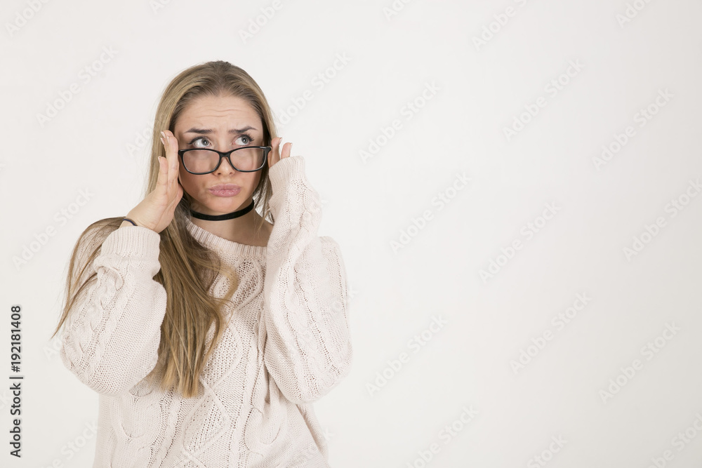 young girl with long hair in glasses and a white knitted sweater looks funny squinting and holding hands with black glasses young girl with long hair in glasses and a white knitted sweater looks funny squinting and holding hands with black glasses