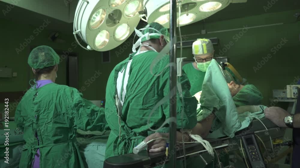 Team of senior surgeons together with female medical assistants using surgical tools to performing surgery operation of mature patient under anesthesia on table at operating theater,indoors,dolly shot Team of senior surgeons together with female medical assistants using surgical tools to performing surgery operation of mature patient under anesthesia on table at operating theater,indoors,dolly shot