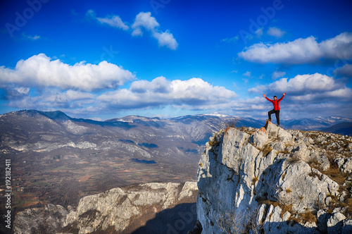 Young man on a cliff edge on the top of mountain with gorgeous view. Hiker on mountain peak on beautiful sunny day