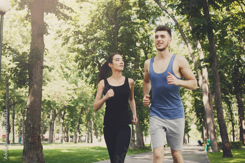 Young woman and man jogging in green park, copy space