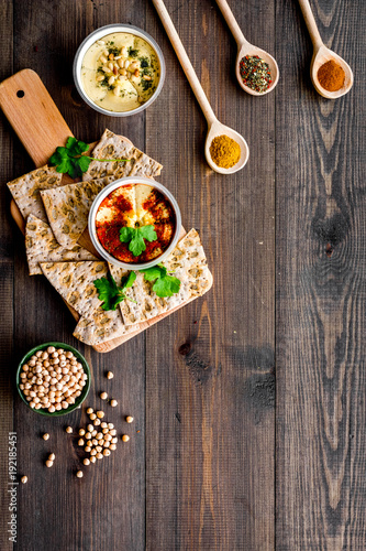 Serve hummus. Bowl with dish near pieces of crispbread on dark wooden background top view copy space