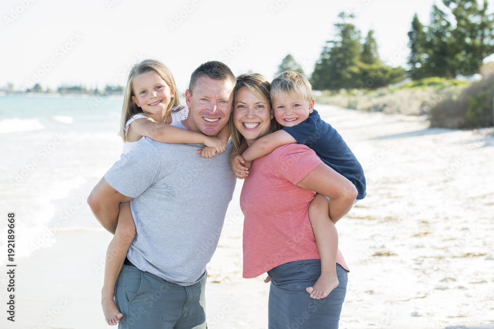 young happy beautiful family having holidays on beach smiling mom and dad carrying little son and young daughter on the back young happy beautiful family having holidays on beach smiling mom and dad carrying little son and young daughter on the back