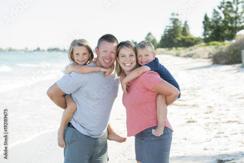 young happy beautiful family having holidays on beach smiling mom and dad carrying little son and young daughter on the back