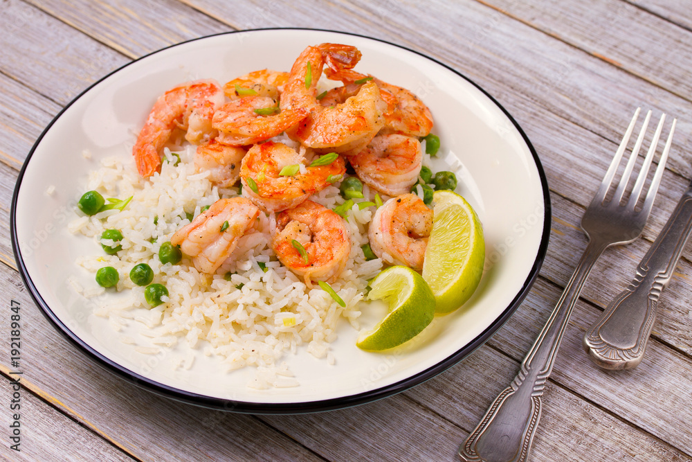Shrimps with ginger rice and green peas, lime on white plate on wooden background Shrimps with ginger rice and green peas, lime on white plate on wooden background