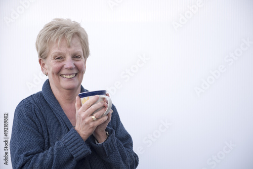 Smiling mature woman holding a cup of coffee, with copy space 